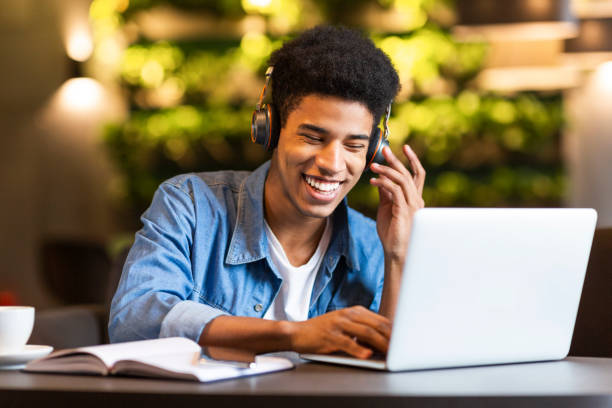Cheerful black young guy with headset looking at laptop