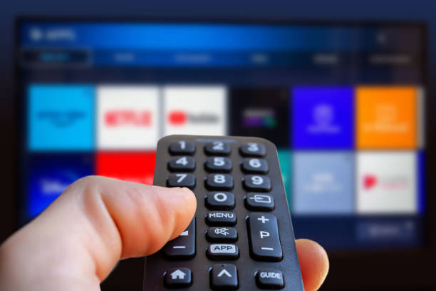 A man is holding a remote control of a smart TV in his hand. 