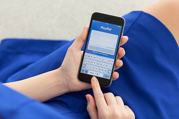Woman holding a phone with service PayPal on the screen. 